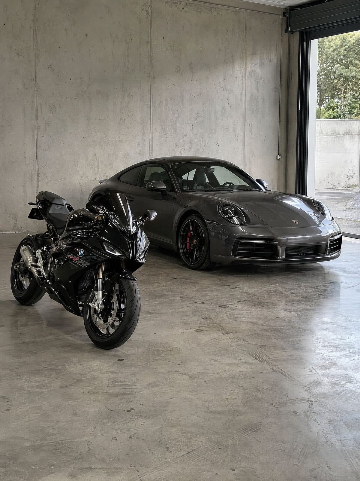 Porsche 911 grafite e BMW S 1000 RR preta em garagem de concreto